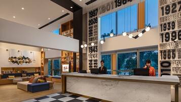A modern hotel lobby with a checkered floor, a reception desk, and a seating area with a sofa and bookshelves.