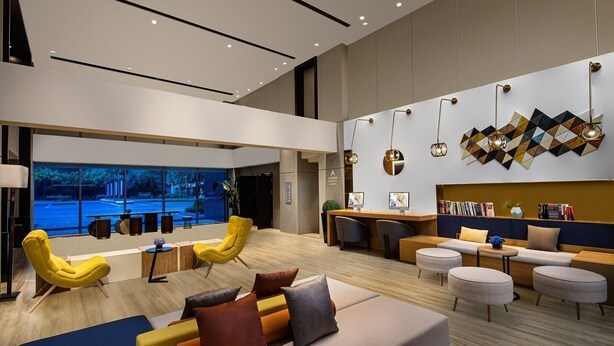 A modern hotel lobby with a reception desk, seating areas, and a view of the outside.