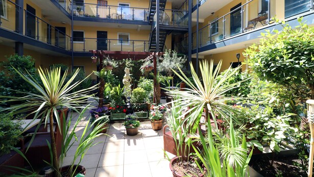 Un atrio de varios niveles con balcones, plantas en macetas y una escalera central.
