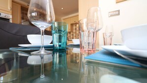 Una mesa de comedor con cristalería y platos, un sofá negro y una cocina al fondo.