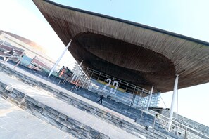 A modern architectural structure with a large, slanted roof and a staircase leading up to it. - 3 Bed Apartment - Mermaid Quay (Cardiff)