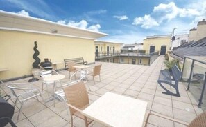 A rooftop terrace with outdoor seating, including tables and chairs, and a view of surrounding buildings. - 3 Bed Apartment - Mermaid Quay (Cardiff)