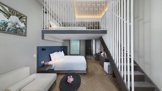A modern hotel room with a bed, a sofa, a coffee table, and a staircase.