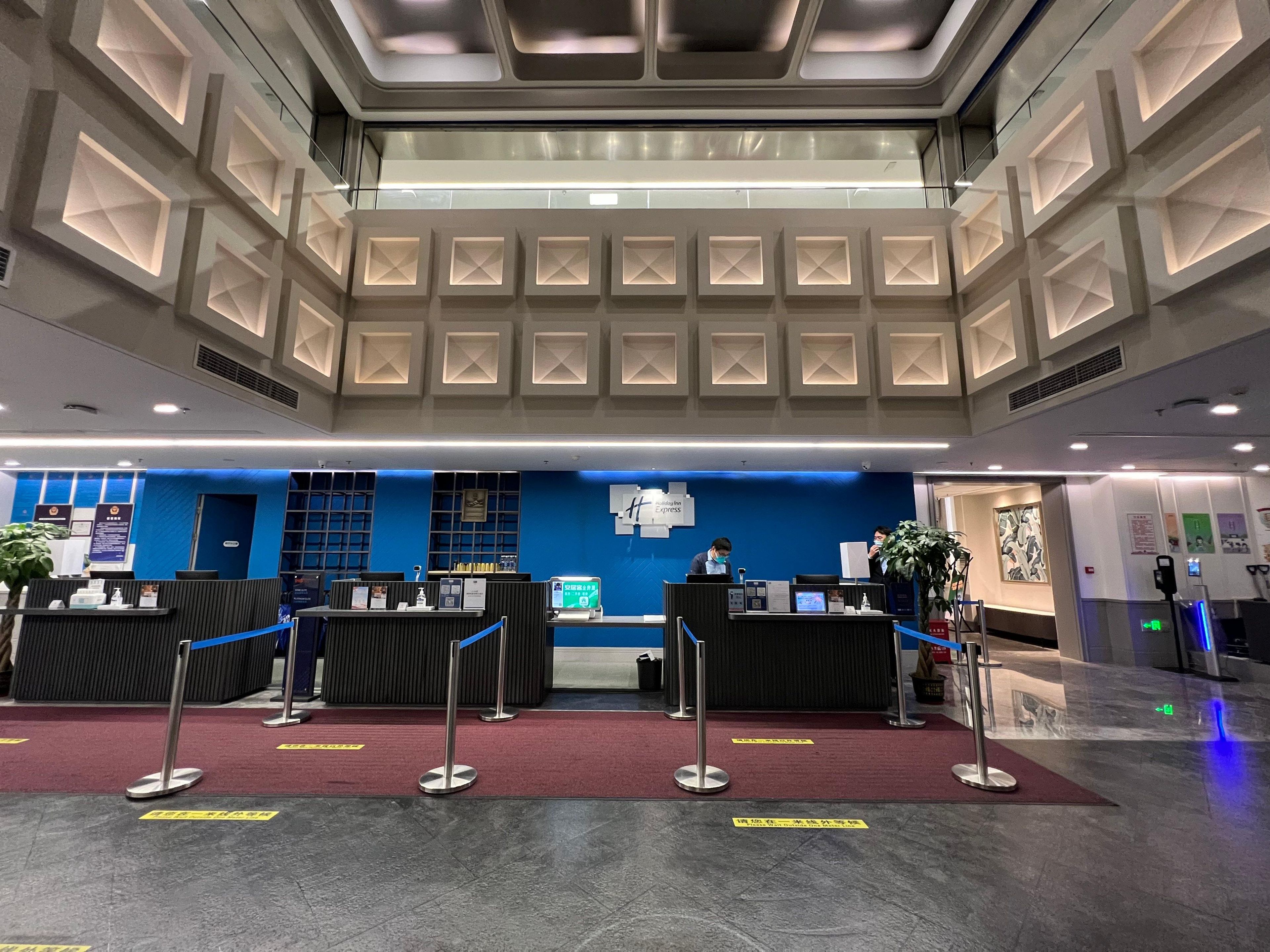 A hotel reception area with a modern design, featuring a blue accent wall, a reception desk, and a digital information board.