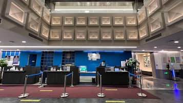 A hotel reception area with a modern design, featuring a blue accent wall, a reception desk, and a digital information board.