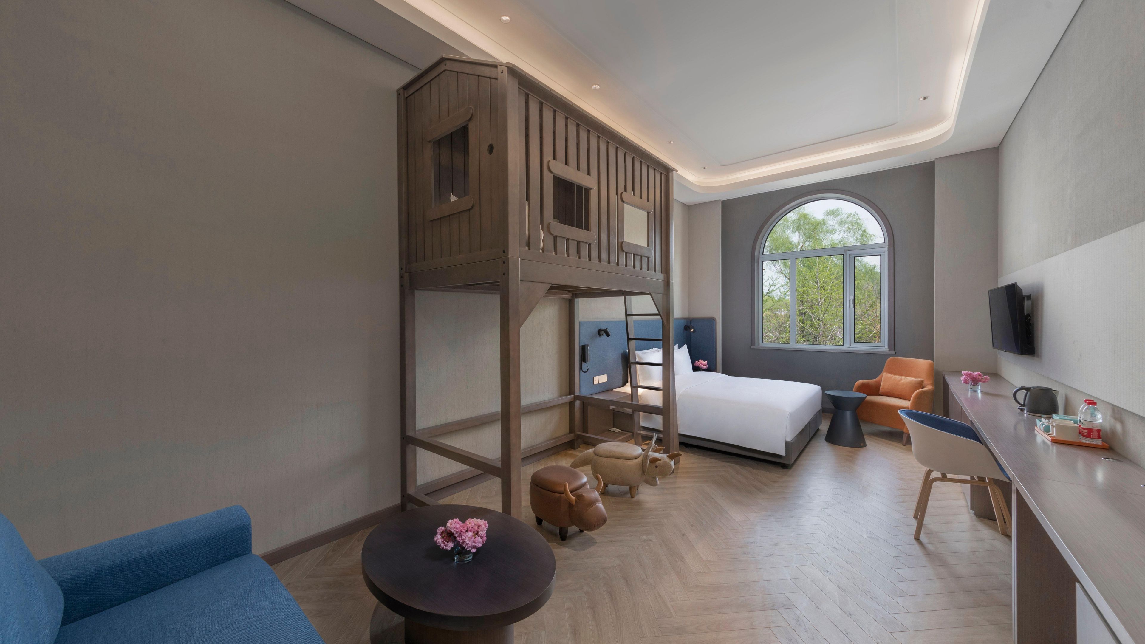 Una moderna camera d'albergo con un letto a castello, una scrivania, una sedia, un tavolo rotondo con un vaso e una grande finestra.