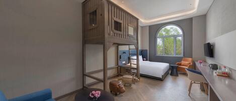 A modern hotel room with a bunk bed, a desk, a chair, a round table with a vase, and a large window.