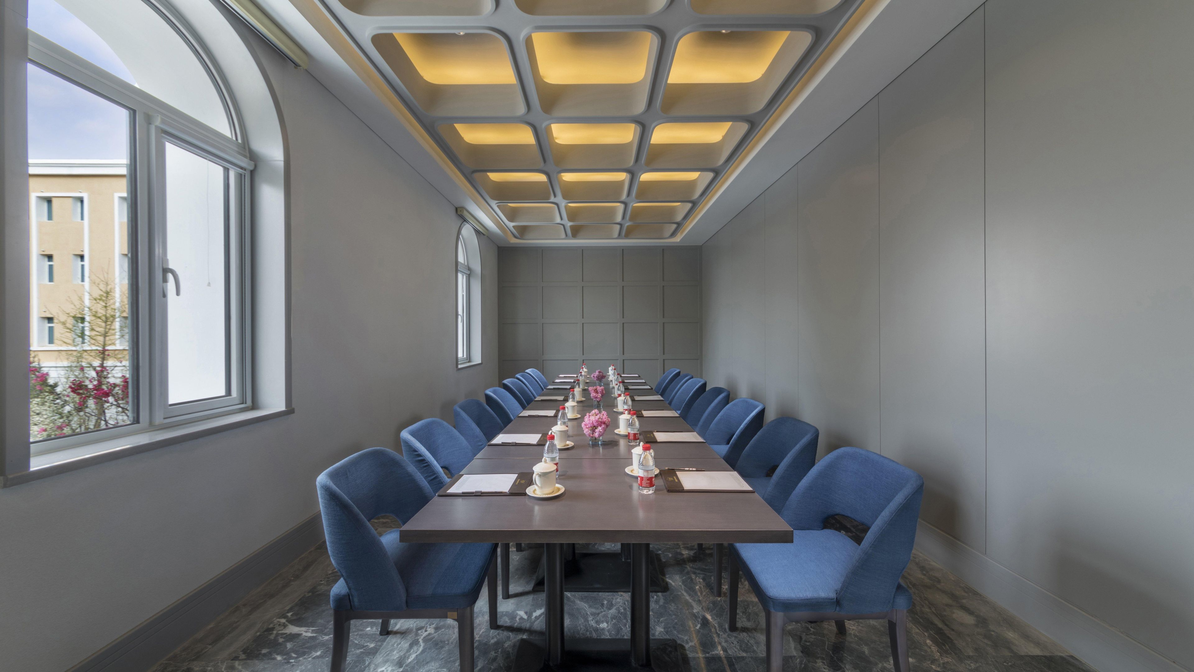 A conference room with a long table, blue chairs, and a modern ceiling design.