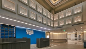 A modern hotel lobby with a blue accent wall, a reception desk, and a geometric ceiling design.