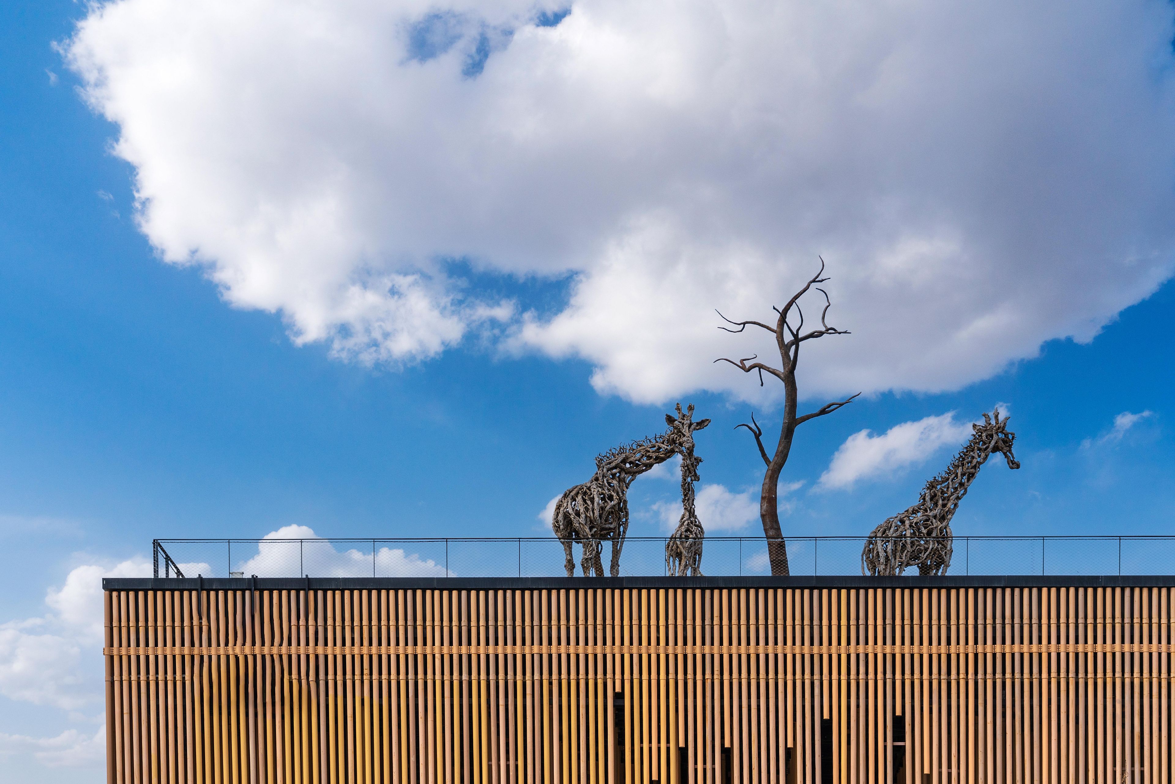 Ein Gebäude mit Bambusfassade und drei Giraffenskulpturen.