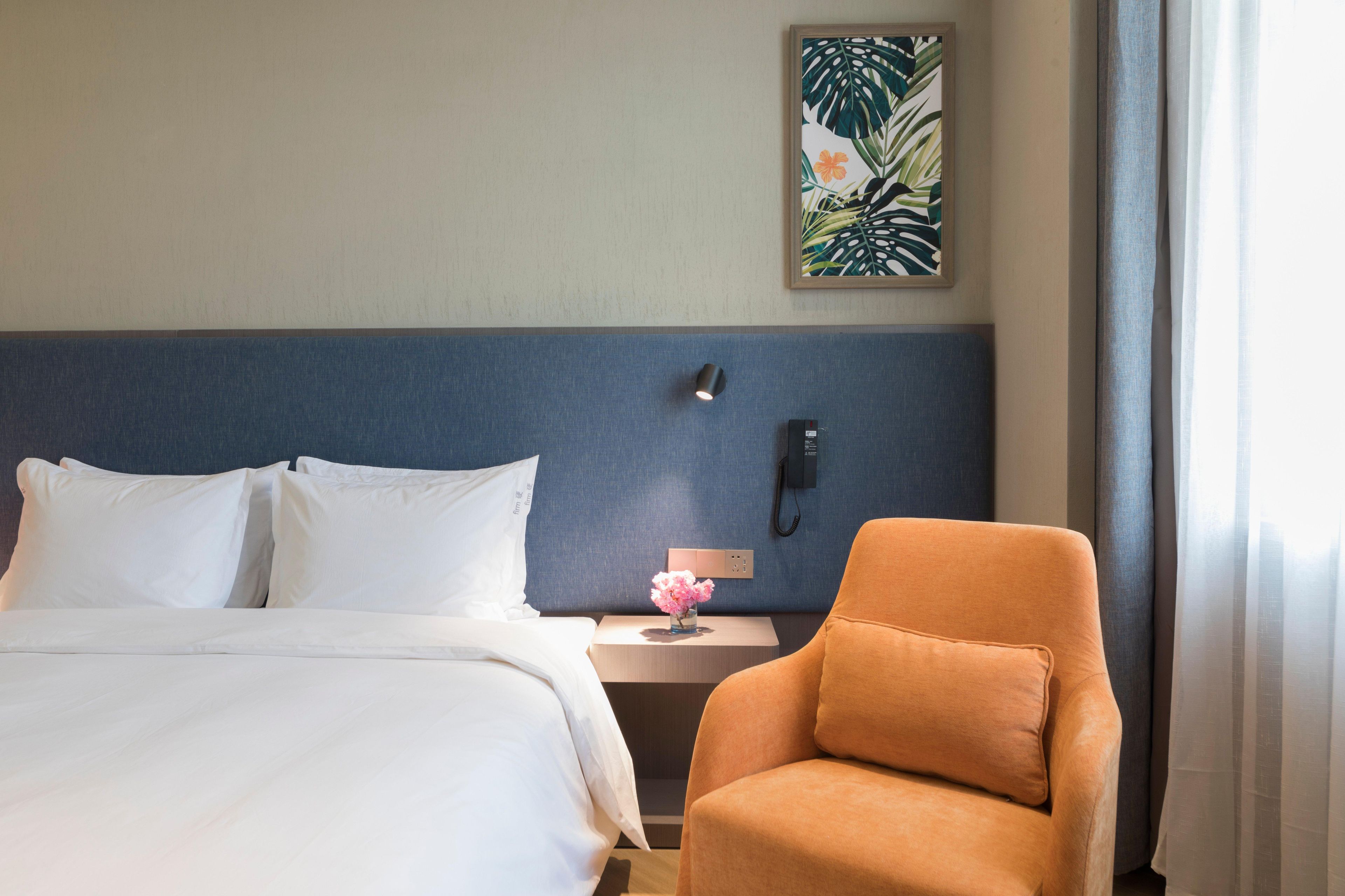 A hotel room with a bed, a nightstand, a phone, a chair, and a wall art piece.
