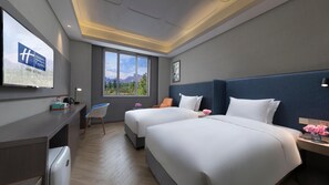 Une chambre d’hôtel avec deux lits, un bureau, une chaise, une fenêtre donnant sur la montagne et un téléviseur fixé au mur.