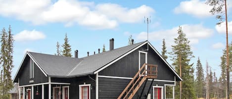 En tvåvånings timmerstuga med en veranda, en skorsten och en trätrappa.
