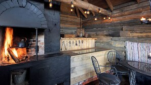Et rustikt interiør med en brændeovn, metalstole, et træbord og en hængende lampe.