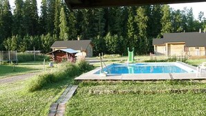 Une piscine entourée d’une terrasse en bois, de pelouse et d’arbres.
