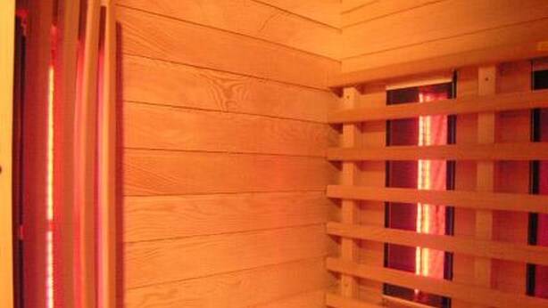 Une pièce en bois avec une fenêtre à persiennes, un lit avec une literie à rayures et un luminaire rouge.