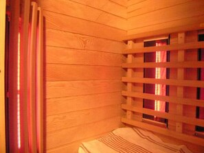 Ein Zimmer mit Holzboden, einem Fenster mit Lamellen und einem Bett mit gestreifter Bettwäsche, darüber ein rotes Licht.