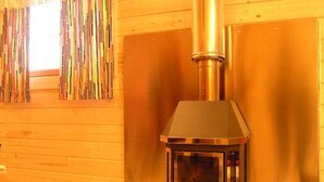 Un poêle à bois se trouve dans une pièce dont les murs sont en bois et qui possède une fenêtre avec des rideaux.