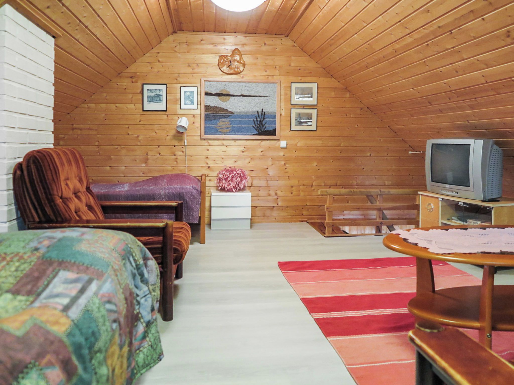 Un dormitorio acogedor en el ático con cama, una silla, una mesita, un televisor y un cuadro en la pared.