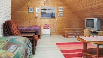 Un dormitorio acogedor en el ático con cama, una silla, una mesita, un televisor y un cuadro en la pared.