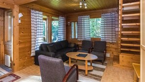 Accogliente interno di una baita con arredamento in legno, un divano, due poltrone, un tavolino e una scala.