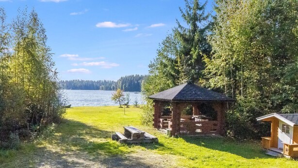 Un rifugio sul lago con tavolo da picnic e un piccolo ripostiglio, circondato da alberi fitti e vista aperta sul lago.