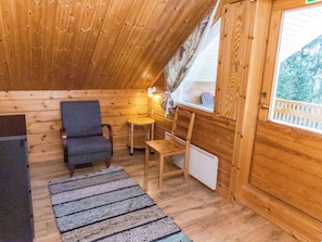 A cozy cabin interior with wooden walls, a gray chair, a small table, a radiator, and a window with a view of trees. - Rinnepelto by Interhome (Nilsiä)