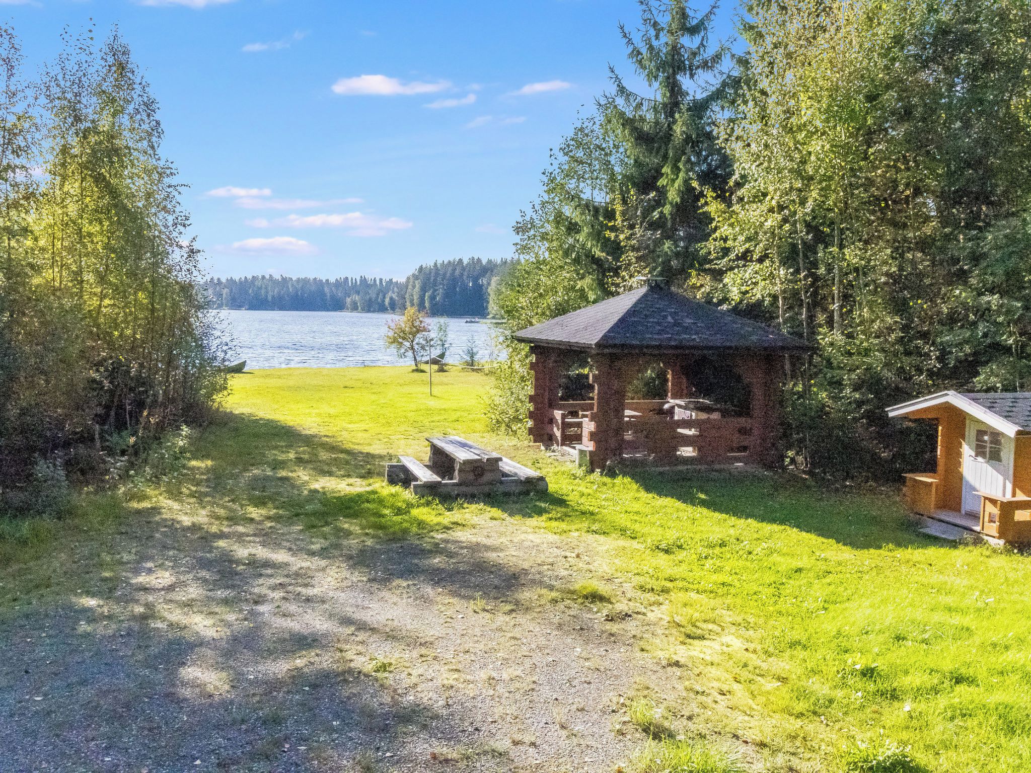 A cabin with a small deck, surrounded by a grassy area and trees, near a body of water.