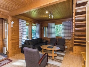 A cozy cabin interior with a sofa, chairs, a small table, and a staircase. - Rinnepelto by Interhome (Nilsiä)
