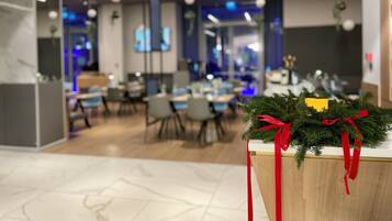 Un espacio interior moderno con mesas y sillas, un árbol de Navidad adornado con lazos rojos y un letrero que anuncia una oferta.