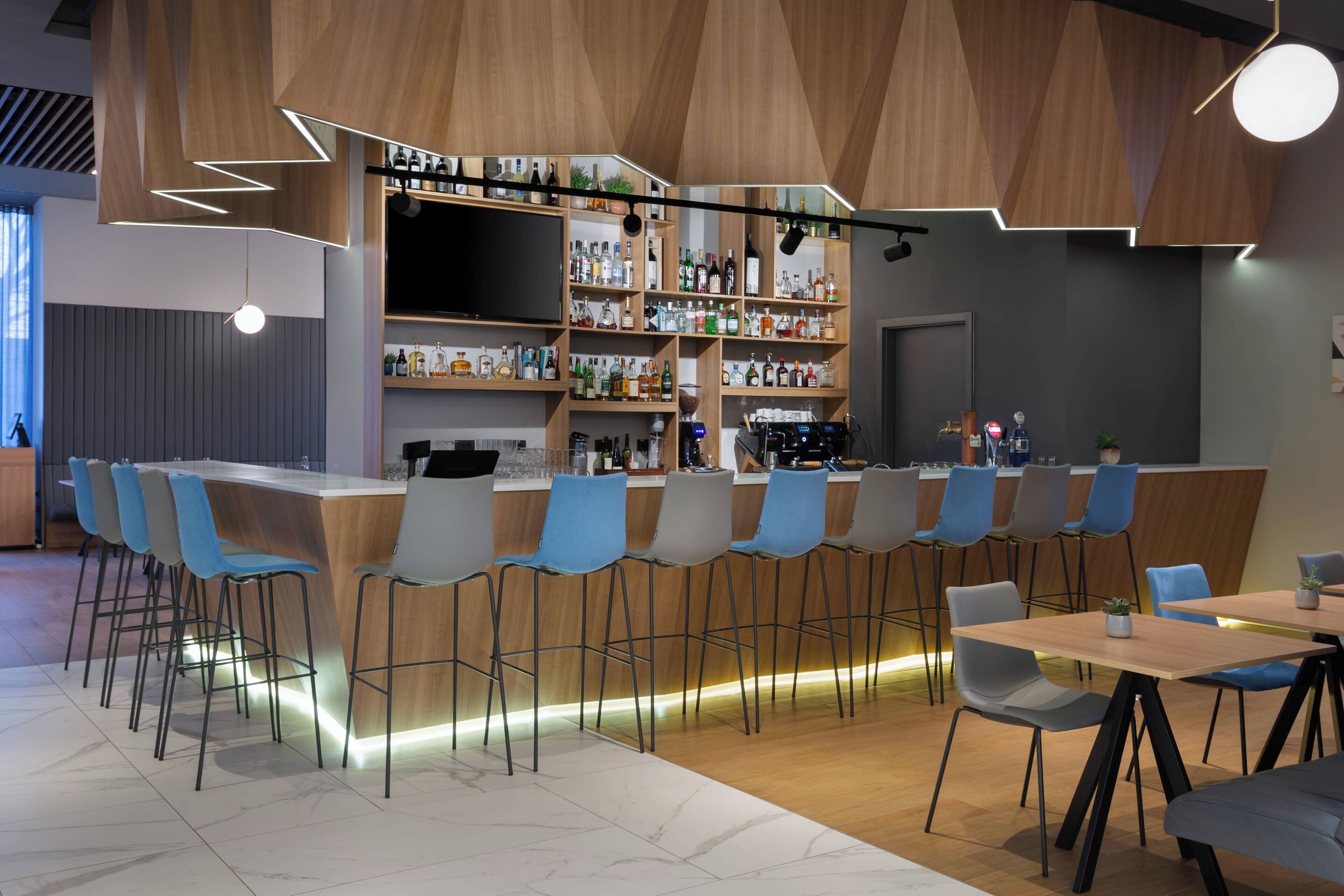 A modern bar area with a long counter, multiple seating options, and a variety of bottles on shelves.