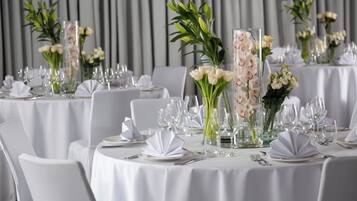 A banquet hall with round tables set for a formal event, featuring white tablecloths, glassware, and floral centerpieces.