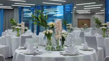 Une salle de banquet avec des tables rondes dressées pour le repas, chacune étant recouverte d’une nappe blanche et agrémentée de verres et de compositions florales.