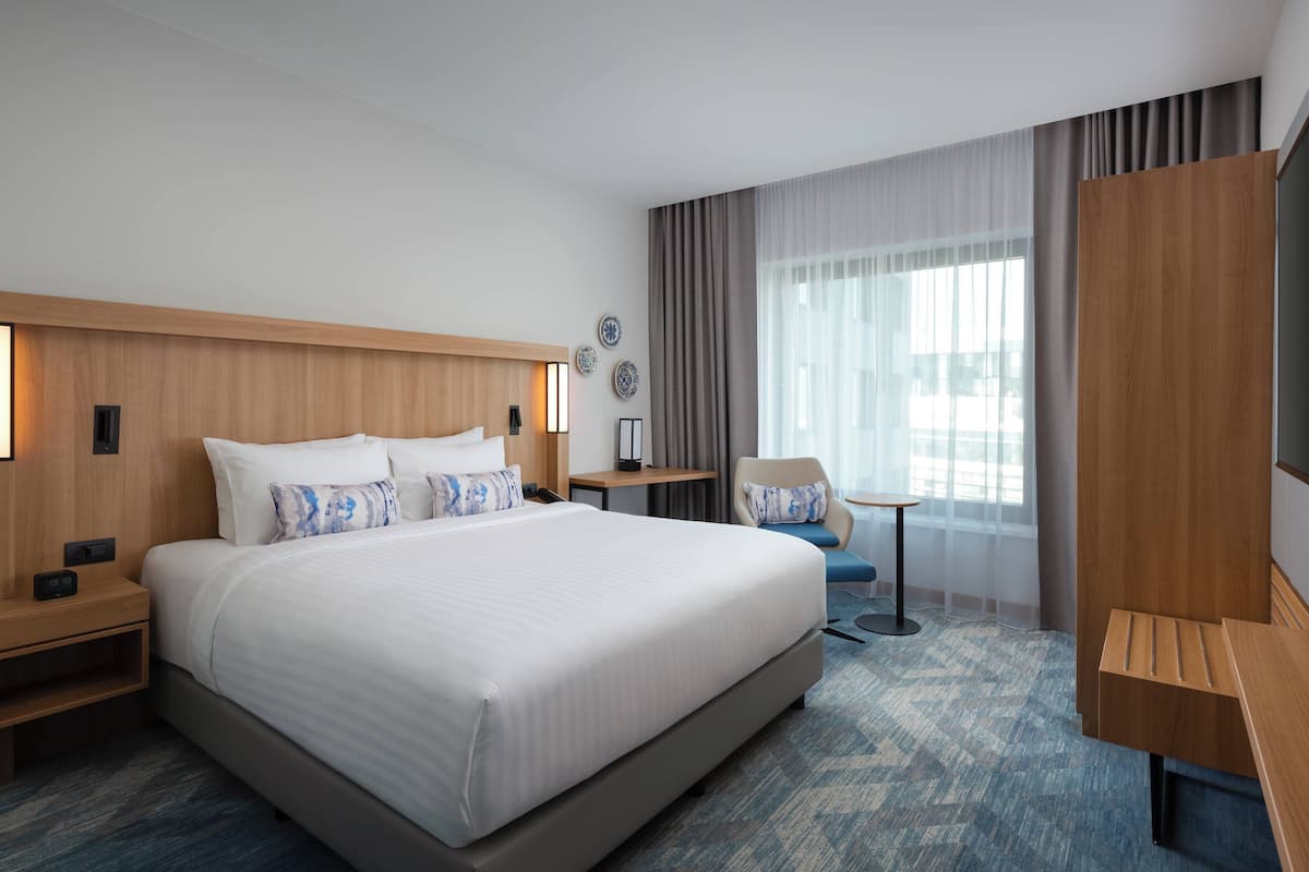Ein modernes Hotelzimmer mit einem großen Bett, einem Schreibtisch, einem Stuhl und einem Fernseher.