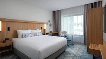 A modern hotel room with a large bed, a desk, a chair, and a TV.