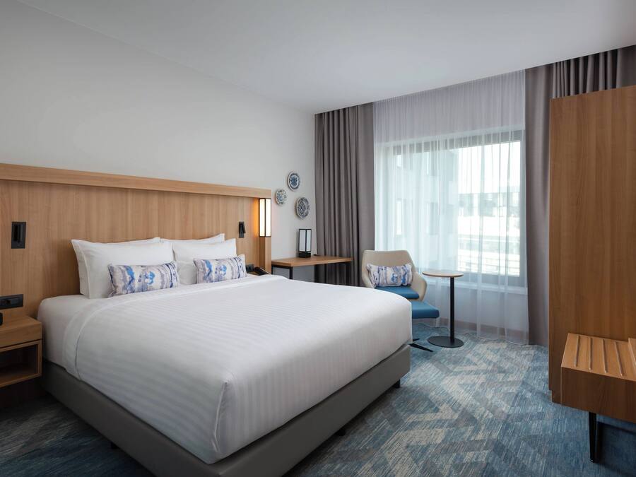 A modern hotel room with a large bed, a desk, a chair, and a TV.