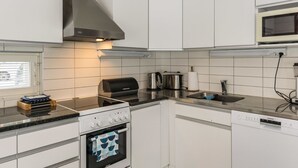 Une cuisine moderne avec des armoires blanches, une hotte de cuisinière en acier inoxydable, un four encastré, un four à micro-ondes et un lave-vaisselle.
