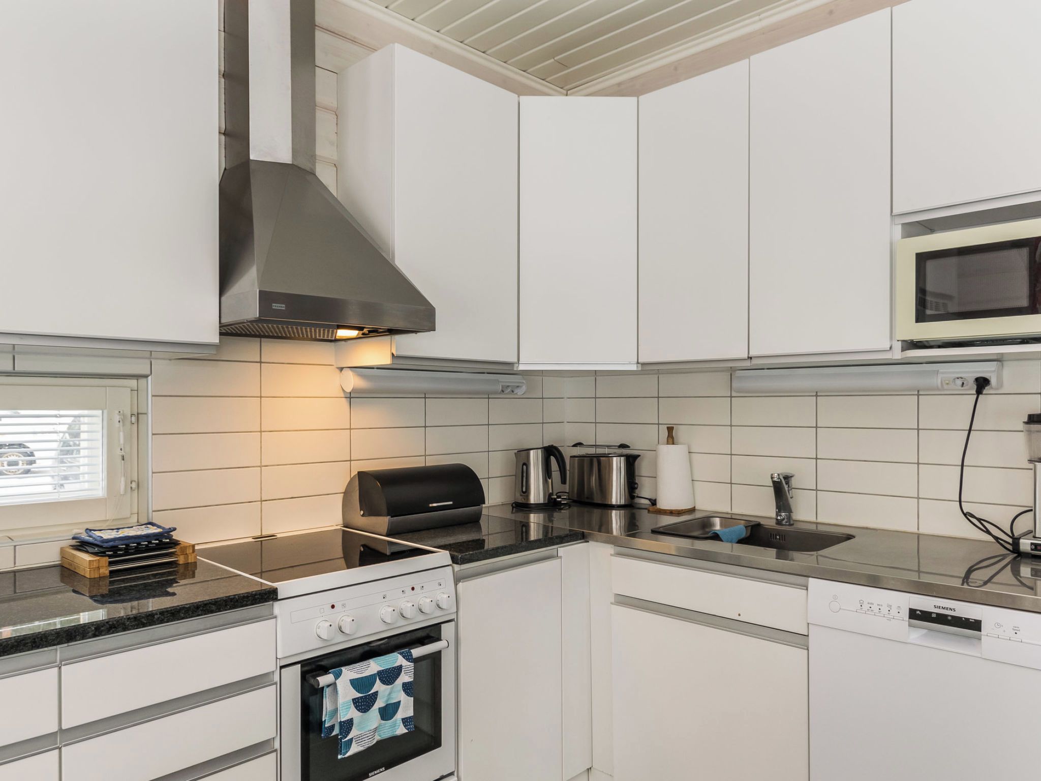 Een moderne keuken met witte kasten, een roestvrijstalen afzuigkap, een inbouwmagnetron en een Siemens vaatwasser.