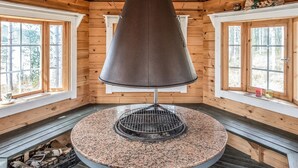 Une pièce aux murs lambrés, avec un grand poêle rond en métal placé au centre, de grandes fenêtres et un plafond en bois.