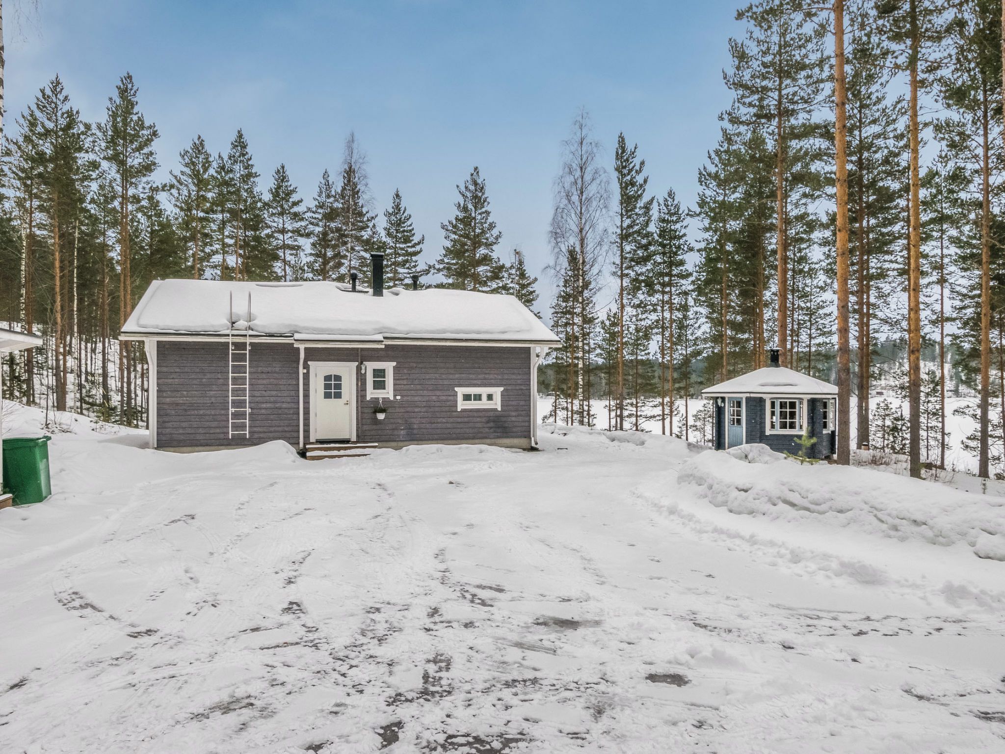 Une cabane à deux étages, dont le toit est recouvert de neige, entourée de grands pins.