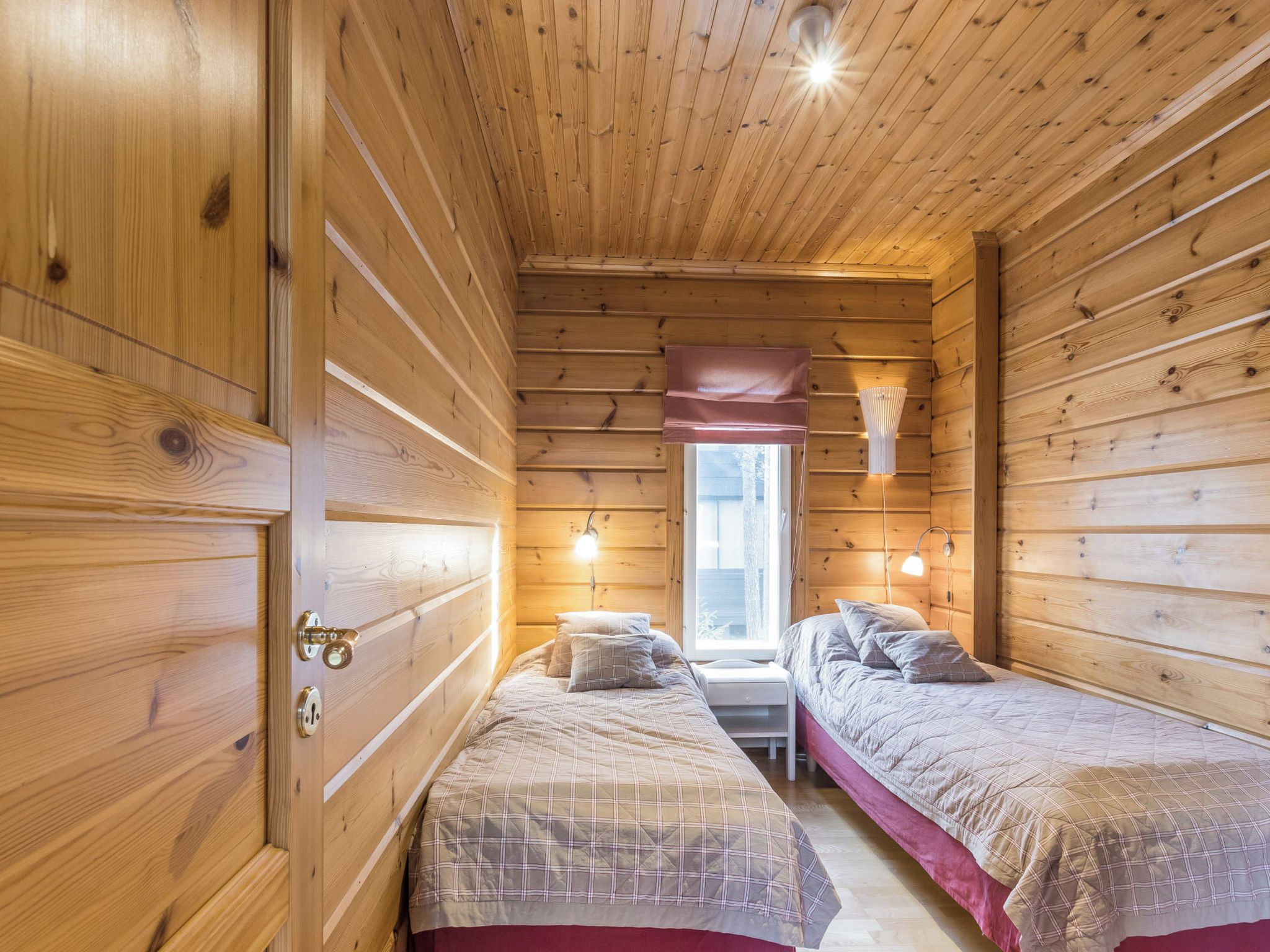 A cabin with two beds, wooden walls, a window, and a ceiling light.