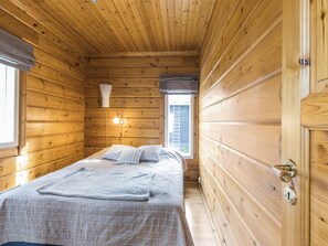 Ein schmaler Raum mit Holzboden, einem Bett, einem Fenster und einer Tür.