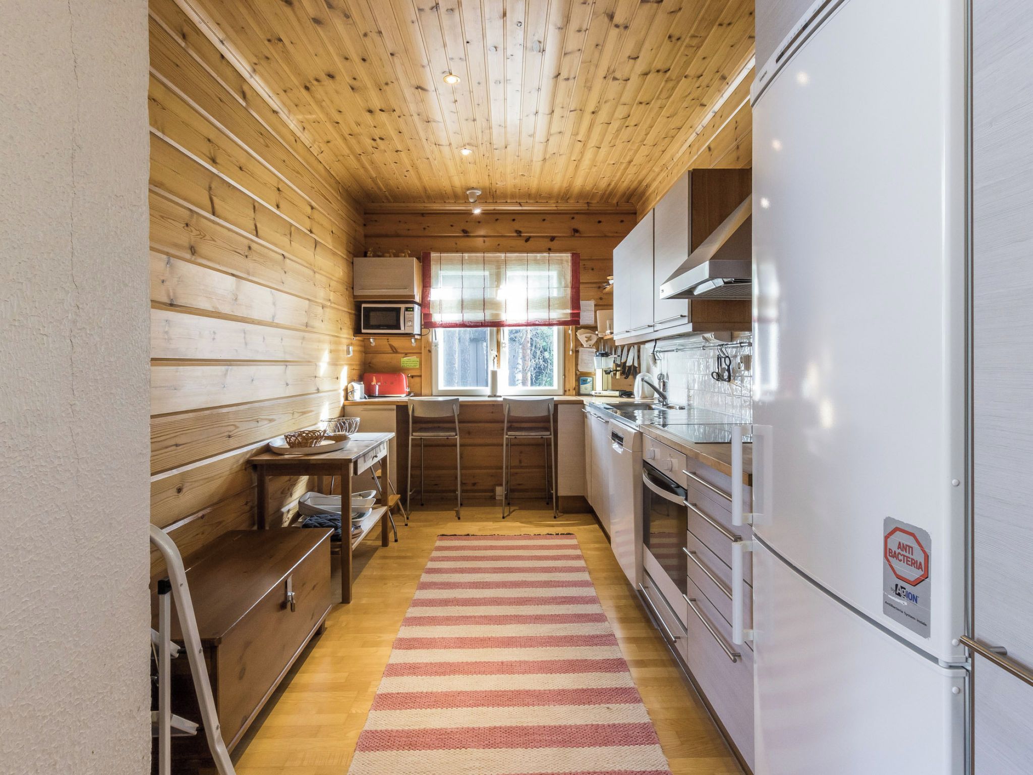 A compact kitchen with wooden walls, a microwave, a refrigerator, and a window with a view.
