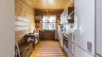 A compact kitchen with wooden walls, a microwave, a refrigerator, and a window with a view.