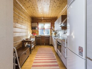 A compact kitchen with wooden walls, a microwave, a refrigerator, and a window with a view.