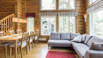 Et interiør i træ med spiseområde, sofa og store vinduer.