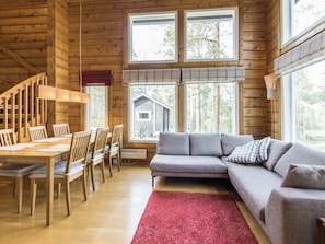 A wooden interior with a dining area, sofa, and large windows.