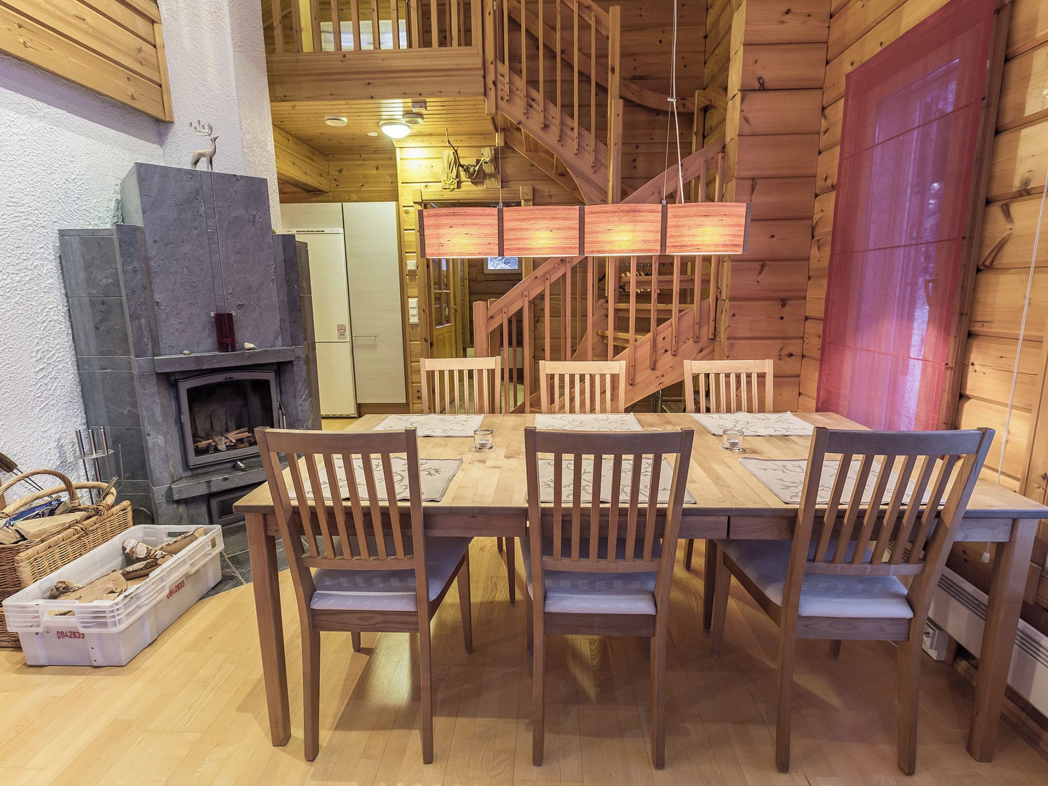 A wooden interior with a dining table, chairs, a fireplace, and a staircase.