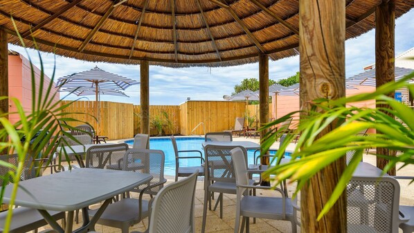 A poolside area with a thatched roof, lounge chairs, and a pool. - Osprey Holiday Village Unit 122/2 Bedroom apartment in complex with a pool (EXMOUTH)
