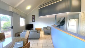 A modern living room with a flat-screen TV, grey sofas, a wicker chair, and a glass table. - Osprey Holiday Village Unit 122/2 Bedroom apartment in complex with a pool (EXMOUTH)